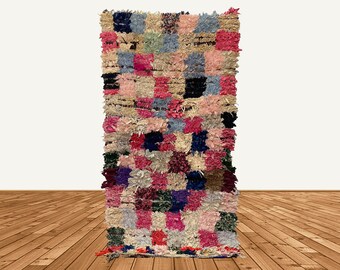 Puede incluir: Una alfombra marroquí colorida con un diseño de patchwork en tonos de rosa, azul, verde y marrón. La alfombra está hecha de lana y tiene un borde con flecos.