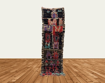 Puede incluir: Una alfombra larga y estrecha, colorida, con un patrón geométrico. La alfombra está hecha de lana y tiene flecos en ambos extremos. La alfombra es de varios colores, incluyendo rojo, azul, verde y negro.