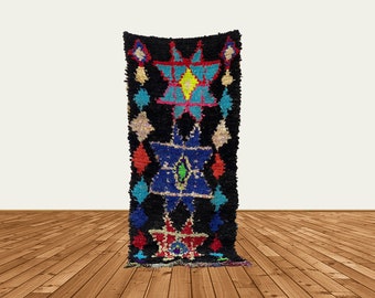 Puede incluir: Una alfombra marroquí negra y colorida con un patrón geométrico de estrellas y diamantes. La alfombra está hecha de lana y tiene una textura tejida a mano.