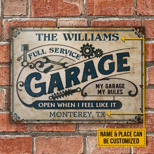 Op de afbeelding: Een vintage-stijl garageschild met de tekst "The Williams Full Service Garage" in blauwe en witte letters. Het bord bevat ook de tekst "My Garage My Rules" en "Open When I Feel Like It". Het bord is op een bakstenen muur achtergrond.