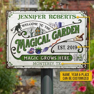 May include: A white metal sign with green lettering that reads "Welcome to the Magical Garden, Est. 2019, Magic Grows Here, Monterey, TX". The sign features a black cat, a witch's hat, a cauldron, a broom, and a mortar and pestle.