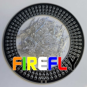 May include: A black circular circuit board with a ring of LEDs around the edge. The board has the word "FIREFLY" printed on it in rainbow colors. A pile of clear LED lights are in the center of the board.