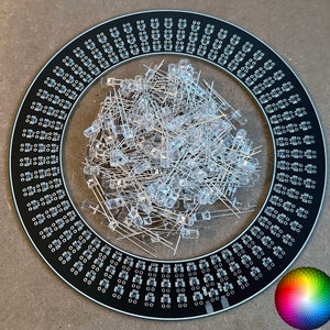 May include: A black circular circuit board with a ring of small holes around the edge. A pile of clear LED lights are in the center of the board. A color wheel is in the lower right corner of the image.