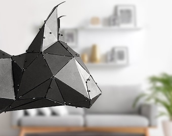May include: A geometric, black metal sculpture of an animal head, possibly a bull or a similar horned creature. The sculpture is constructed from multiple triangular and polygonal pieces, joined together with small rivets. The artwork is displayed against a blurred interior background.