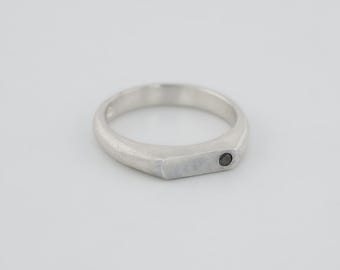May include: A silver ring with a black diamond set in the center of the band.