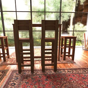 May include: A dining set with a rectangular table and four matching chairs. The chairs have a ladder-back design. Two smaller stools are also present. The set is made of dark wood and sits on a patterned rug.