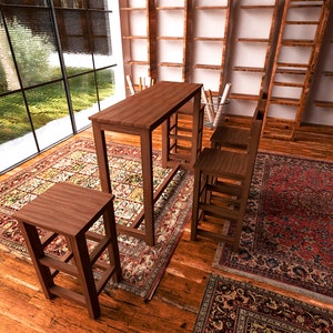 May include: A wooden bar table and two matching stools are set on a patterned rug in a room with large windows and bookshelves. The table and stools are a warm brown color, and the rug has a red and beige design.