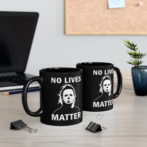 May include: Two black ceramic mugs with white text and a graphic of a horror movie character. The text on the mugs reads "No Lives Matter".