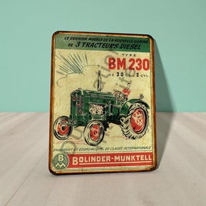 May include: Vintage metal sign featuring a green tractor with red wheels and the text "BM 230". The sign has a distressed, aged appearance with French text at the top and the Bolinder-Munktell logo at the bottom. The sign is rectangular.