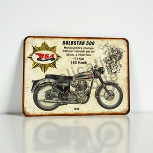 May include: A vintage-style metal sign featuring a BSA Goldstar 500 motorcycle illustration. The sign includes technical specifications and the year 1956. The sign has a distressed, aged appearance with a white background.