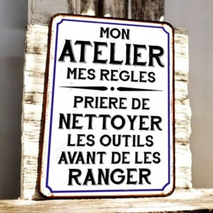 Puede incluir: Un letrero metálico rectangular con fondo blanco y texto negro. El letrero tiene un borde azul y dice: "MON ATELIER MES REGLES PRIERE DE NETTOYER LES OUTILS AVANT DE LES RANGER."