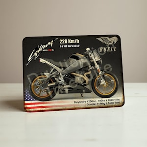 May include: A rectangular metal sign depicting a Buell Lightning XB12S motorcycle. The sign has a black background with the text "Lightning XB12S" and "220 Km/h". The bottom left corner displays the American flag.