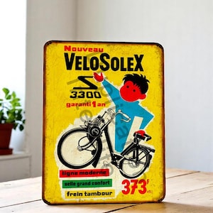 May include: A vintage metal sign with a yellow background, featuring the text "VELOSOLEX" and a moped illustration. The sign includes the text "3300" and "garanti 1 an". The sign also has the text "ligne moderne", "selle grand confort", and "frein tambour".