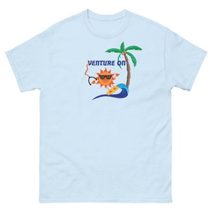 May include: Light blue t-shirt featuring a cartoon sun wearing sunglasses and riding a surfboard. The sun is holding a pair of sunglasses in one hand. The text "Venture On" is above the sun. A palm tree is behind the sun.