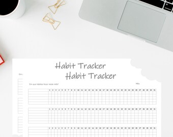 May include: A white habit tracker with the words "Habit Tracker" printed in gray. The tracker has spaces for daily entries and a section to list habits. A laptop, coffee cup, and gold paper clips are also visible.