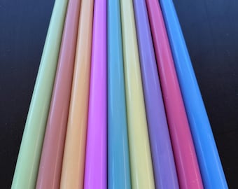 May include: A collection of ten colorful taper candles in a rainbow of pastel shades. The candles are arranged in a fan shape, with colors including green, peach, yellow, pink, and blue. Each candle has a white wick.