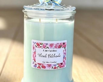 May include: A light blue soy wax candle in a clear glass jar with a glass lid topped by a blue and white striped ribbon bow. The rectangular label features a floral border and the text FJM Candles, Floral Patchouli, Soy Wax Candles.