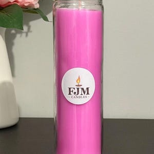 May include: A tall, cylindrical glass jar candle filled with bright pink wax. A circular white label is centred on the front of the glass, featuring a graphic of a lit candle flame above the black text FJM CANDLES in a serif font.