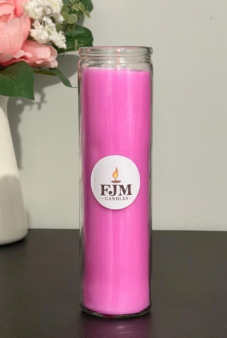 May include: A tall, cylindrical glass jar candle filled with bright pink wax. A circular white label is centred on the front of the glass, featuring a graphic of a lit candle flame above the black text FJM CANDLES in a serif font.