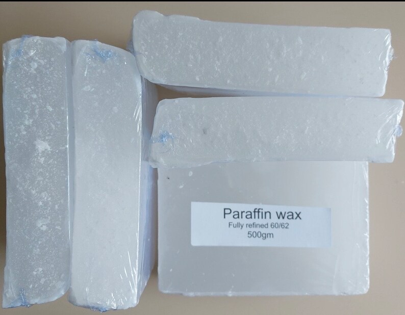 Puede incluir: Cuatro bloques de cera de parafina blanca, cada uno envuelto en pl&aacute;stico transparente. La etiqueta dice "Cera de parafina, Totalmente refinada 60/62, 500g".