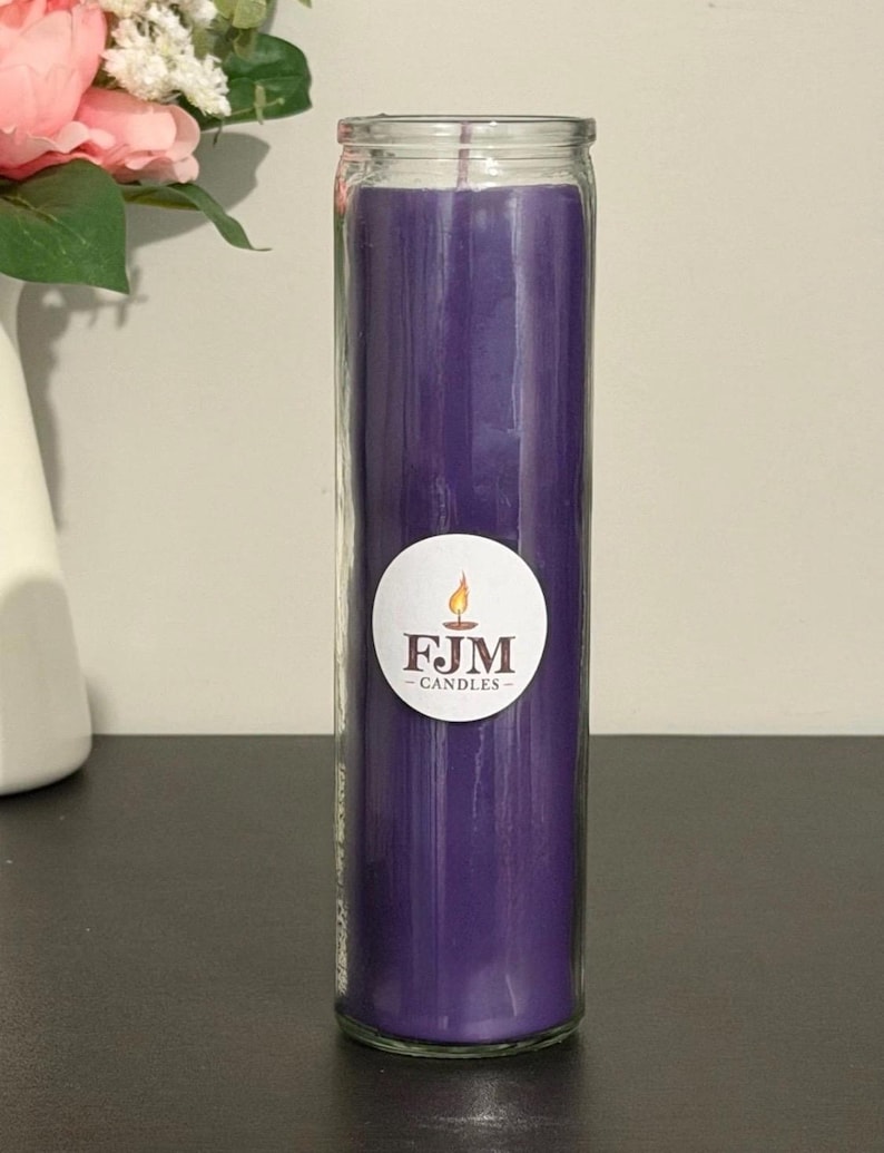 May include: A tall, cylindrical purple candle encased in a clear glass jar. A circular white sticker is centred on the front of the glass, featuring a small orange flame icon above the bold, dark text that reads FJM CANDLES.