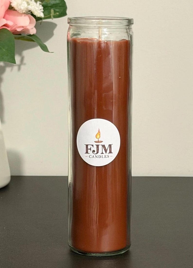 May include: A tall, cylindrical glass candle filled with solid brown wax. A circular white label is centred on the glass, featuring a small flame icon above the bold, dark text "FJM" and the word "CANDLES" printed in smaller letters below.