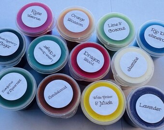 May include: A collection of twelve round plastic containers filled with colorful wax melts. Each lid features a white circular label with black text identifying scents including Rose Victorian, Orange Blossom, Lime & Coconut, Rio De Janeiro, Black Raspberry Sugar, Lemongrass & Ginger, Dragon Blood, Jasmine, Eucalyptus & Spearmint, Sandalwood, White Amber & Musk, and Lavender.
