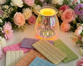 May include: A glass wax warmer with a 3D firework light effect emitting a warm yellow glow, surrounded by several rectangular wax melts in various pastel colors including blue, peach, white, pink, purple, and light green.