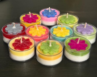 May include: A collection of ten colorful flower-shaped candles in clear plastic containers. The candles feature various colors, including pink, yellow, green, blue, and purple, with white wax bases. Each candle has a central wick.