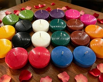 May include: A collection of twenty-one round, flat wax candles in a variety of colors including red, orange, yellow, green, blue, purple, brown, black, and white, each featuring a single centered cotton wick, arranged in a grid-like formation.
