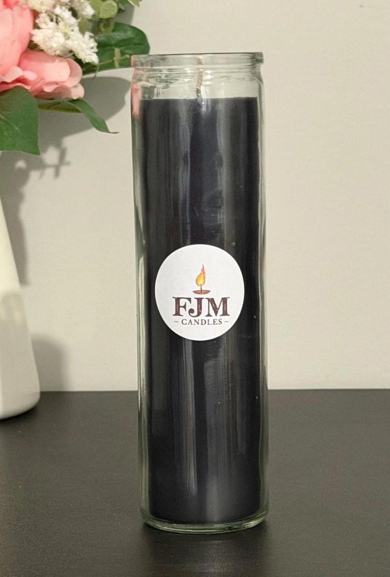 May include: A tall, cylindrical glass candle holder filled with solid black wax. A circular white sticker is centred on the glass, featuring a graphic of a lit candle and the text FJM CANDLES in dark brown lettering with a small flame icon above.