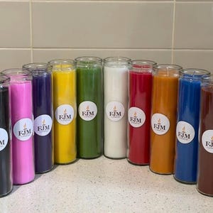 Puede incluir: Una colección de diez velas cilíndricas en frasco de vidrio de varios colores sólidos, incluyendo negro, rosa, morado, amarillo, verde, blanco, rojo, naranja, azul y marrón. Cada vela tiene una etiqueta blanca circular con el texto FJM CANDLES.