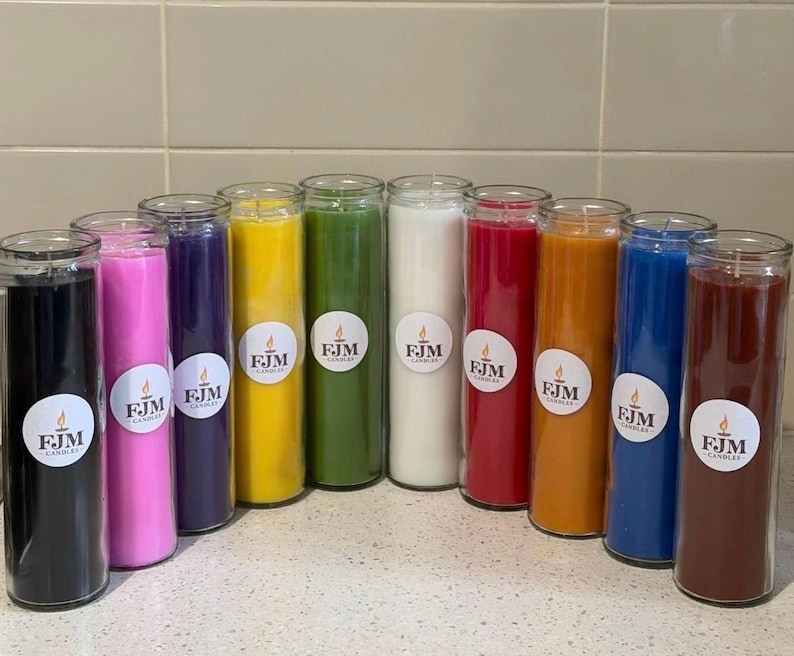 May include: A collection of eleven tall, cylindrical glass prayer candles in various solid colours including black, pink, purple, yellow, green, white, red, orange, blue, and brown. Each candle features a circular white label with the text FJM CANDLES.
