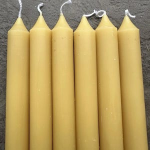Puede incluir: Seis velas cónicas de color amarillo pálido con mechas blancas. Las velas están dispuestas verticalmente, una al lado de la otra, y tienen un cuerpo liso y cilíndrico con una parte superior cónica. Las mechas son visibles en la parte superior de cada vela.