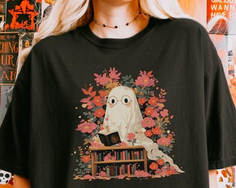 May include: Black t-shirt featuring a whimsical illustration of a ghost wearing glasses and reading a book, surrounded by flowers. The ghost is sitting on a bookshelf. The text "ALL HANDY PRINTABLE" is at the bottom.
