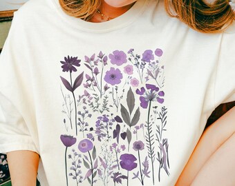 May include: Cream-colored t-shirt featuring a floral design in shades of purple. The graphic includes various flowers and foliage. The text "ALL HANDY PRINTABLE" is visible at the bottom right of the image.