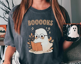 May include: A dark gray t-shirt with the text "BOOOKS" printed on it. A cartoon ghost wearing glasses is reading a book.