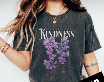 May include: A dark gray t-shirt with a floral design and the text "Be a Kind Human Kindness" printed on the front. The flowers are purple and blue.
