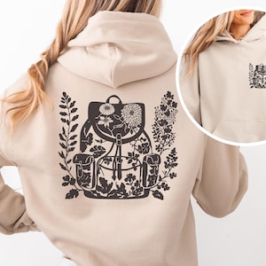 Puede incluir: Sudadera con capucha beige con un diseño de mochila floral negra en la espalda y un diseño más pequeño a juego en la parte delantera. La mochila está llena de flores y rodeada de hojas. El texto "ALL HANDY PRINTABLE" está en la parte inferior.