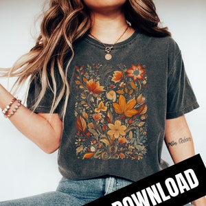 May include: A dark grey t-shirt with a floral print featuring orange, yellow, and red flowers. The flowers are surrounded by green leaves and vines. The text "More Bébé" is visible on the right sleeve of the shirt.