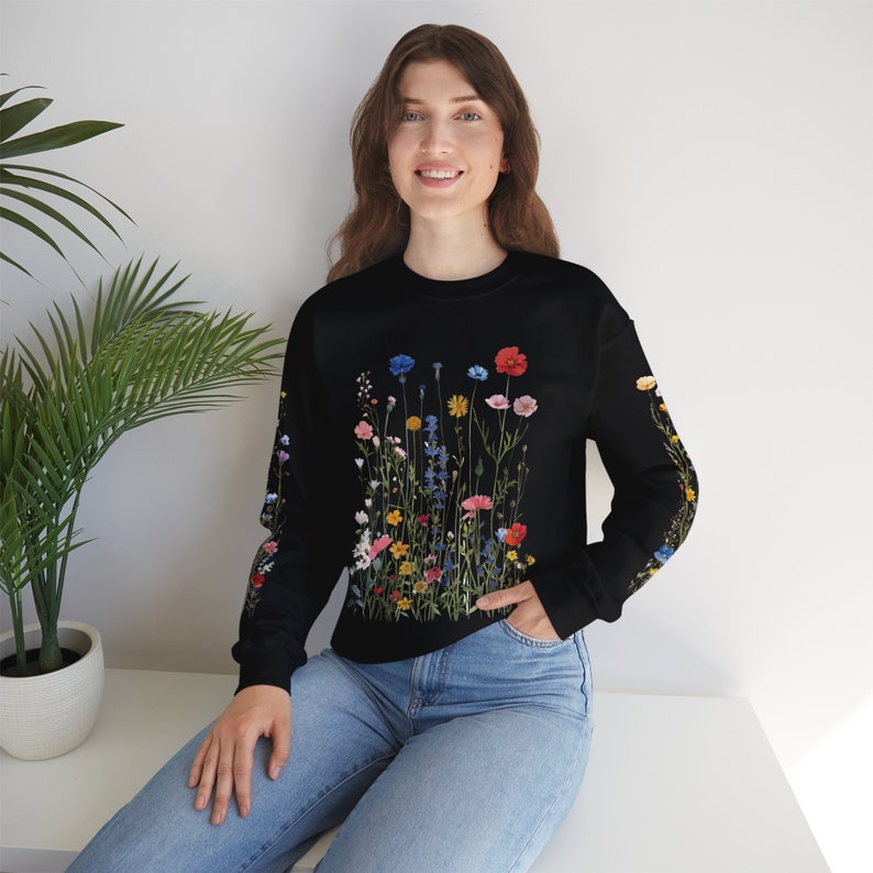 Puede incluir: Una sudadera negra con un estampado floral colorido que presenta una variedad de flores y vegetaci&oacute;n.