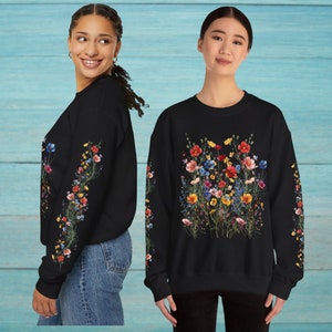 Op de afbeelding: Zwart sweatshirt met een bloemenprint met verschillende kleurrijke bloemen. De bloemen zijn in een cluster in het midden van het sweatshirt en op de mouwen gerangschikt.