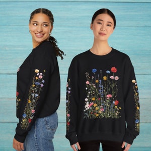 Puede incluir: Dos sudaderas negras con estampado floral. Una sudadera tiene un estampado floral en la manga y la otra tiene un estampado floral en la parte delantera. El estampado floral est&aacute; hecho de varios colores, incluyendo rosa, azul, amarillo y rojo.