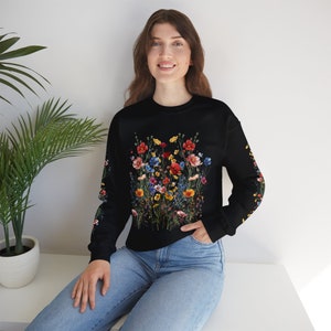 Op de afbeelding: Een zwart sweatshirt met lange mouwen met een kleurrijke bloemenprint. De print bevat een verscheidenheid aan bloemen in tinten rood, geel, blauw en roze.