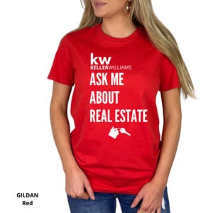 May include: Red Gildan t-shirt with the Keller Williams logo and the text "ASK ME ABOUT REAL ESTATE". The design includes a house and key graphic in white. The shirt is a crew neck style.