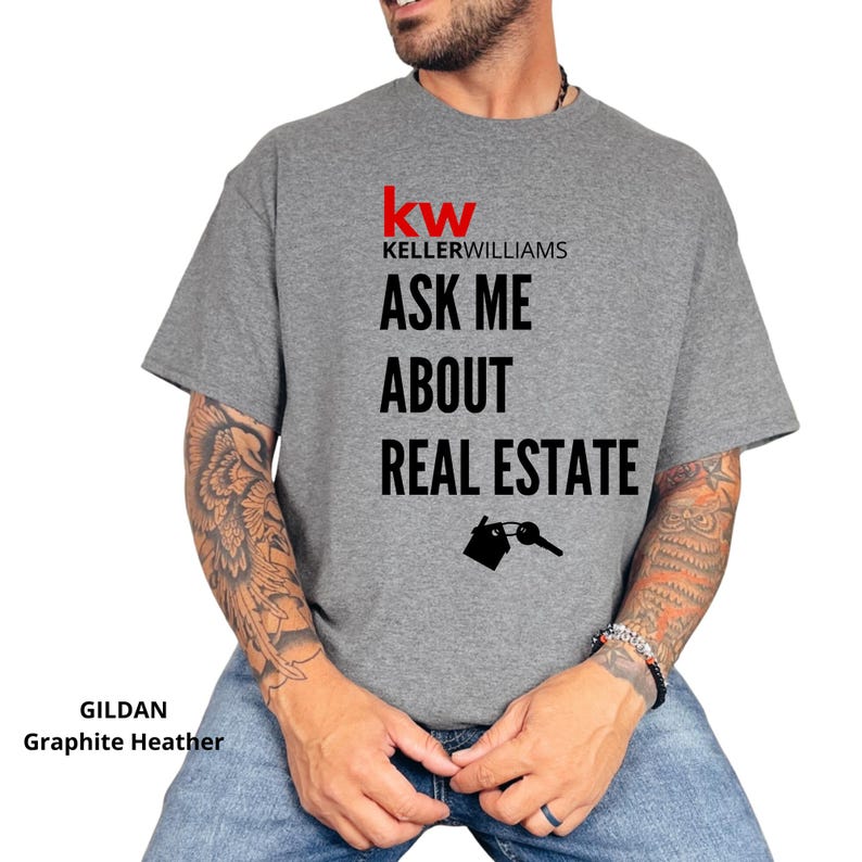 May include: Graphite heather t-shirt with the Keller Williams logo and the text "ASK ME ABOUT REAL ESTATE". The design includes a house and key graphic. The shirt is made of a soft, comfortable material.