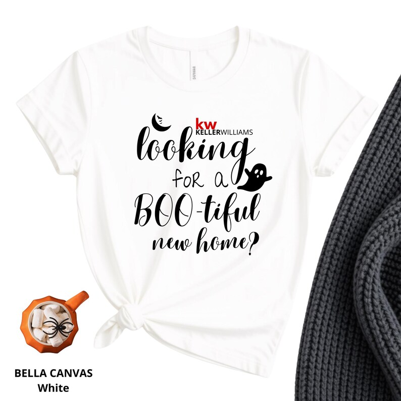 May include: A white short-sleeved t-shirt featuring black text that reads looking for a BOO-tiful new home? with a small ghost and crescent moon graphic. The shirt includes a red and black Keller Williams logo above the text.