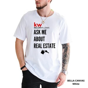 May include: White Bella Canvas t-shirt with the Keller Williams logo and the text "ASK ME ABOUT REAL ESTATE". The design includes a house and key graphic. The shirt is a crew neck.