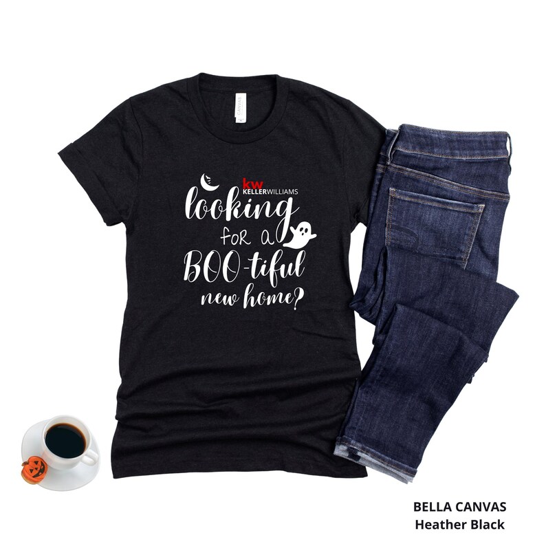 May include: A black short-sleeved t-shirt with white text that reads looking for a BOO-tiful new home? and a small ghost graphic, paired with dark blue denim jeans and a white coffee cup with a small orange pumpkin decoration on the side.