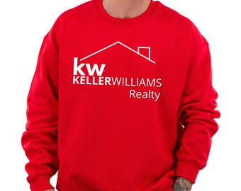 May include: A bright red crewneck sweatshirt featuring a white graphic print on the chest. The design includes a stylized house roof outline above the text 'kw KELLERWILLIAMS Realty'. The garment has long sleeves and a ribbed collar.